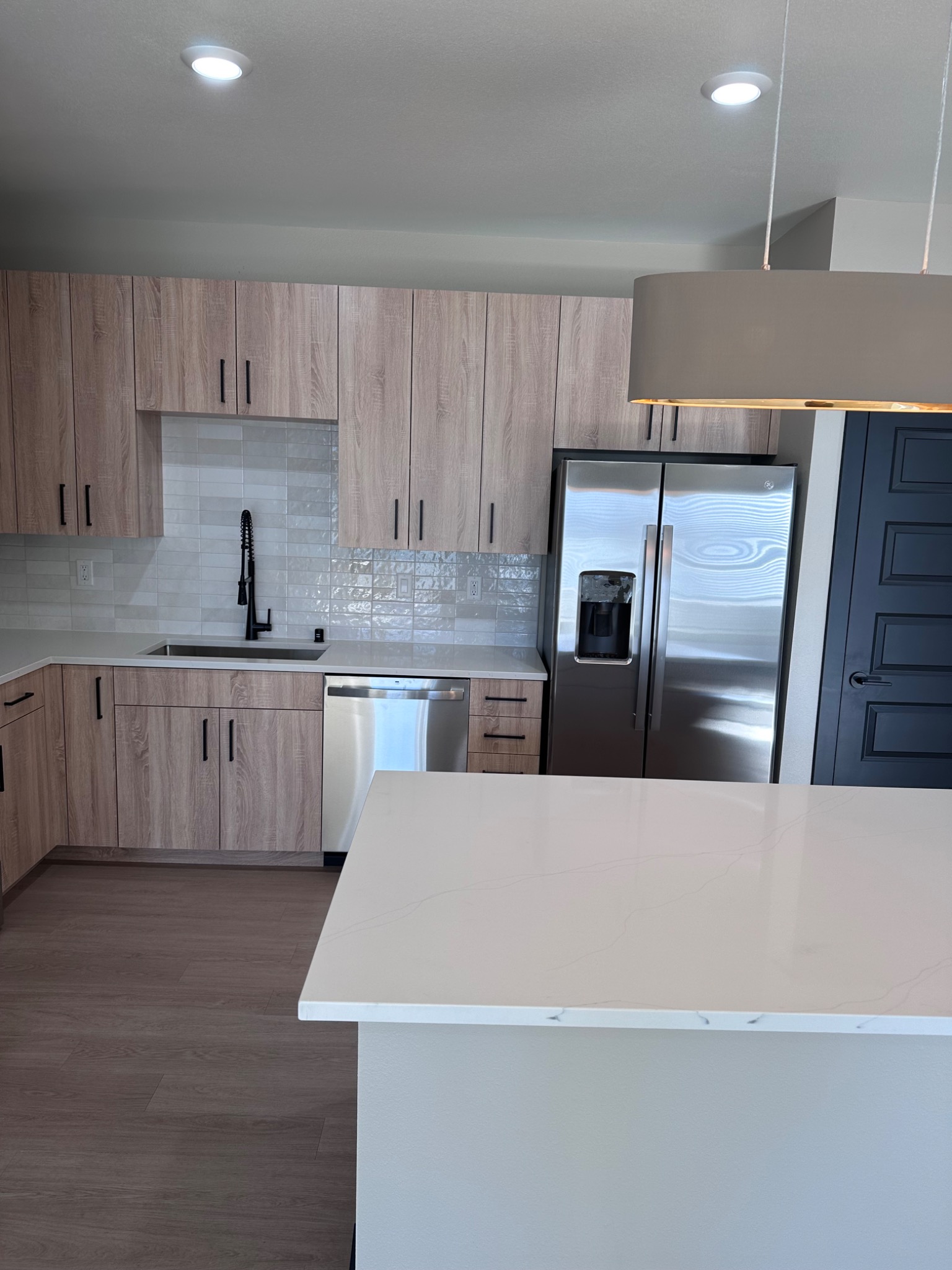 Original photograph of Elysium apartment kitchen with wood-tone cabinetry, stainless steel appliances, and a light-colored island